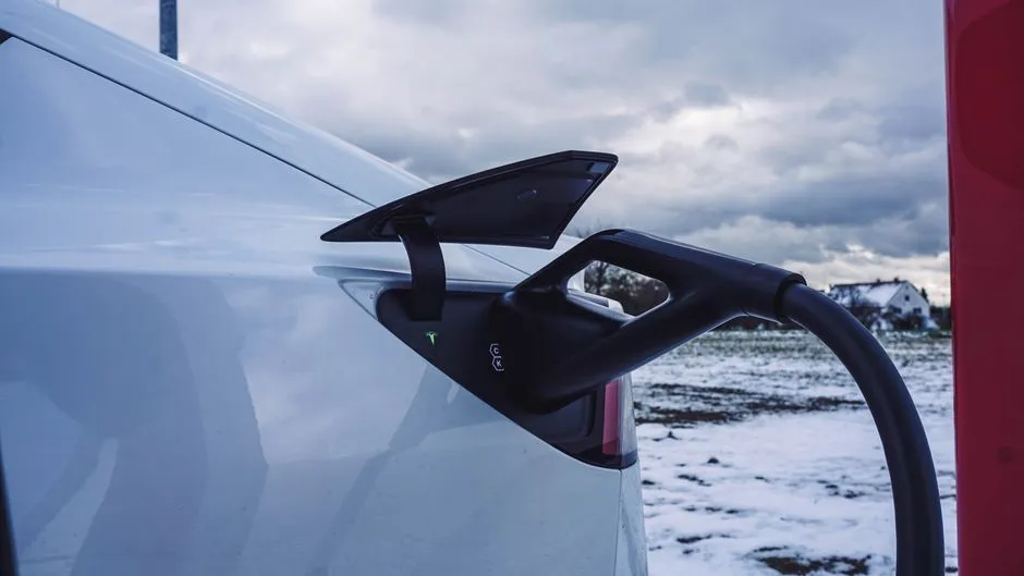 Voiture électrique roulant sur une route enneigée, flocons visibles et batterie affichée au tableau de bord